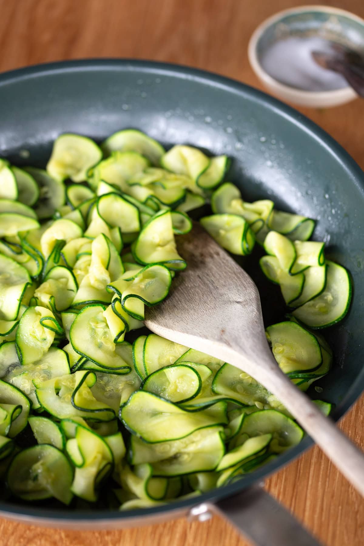 Sliced zucchini being sauteed in a pan.
