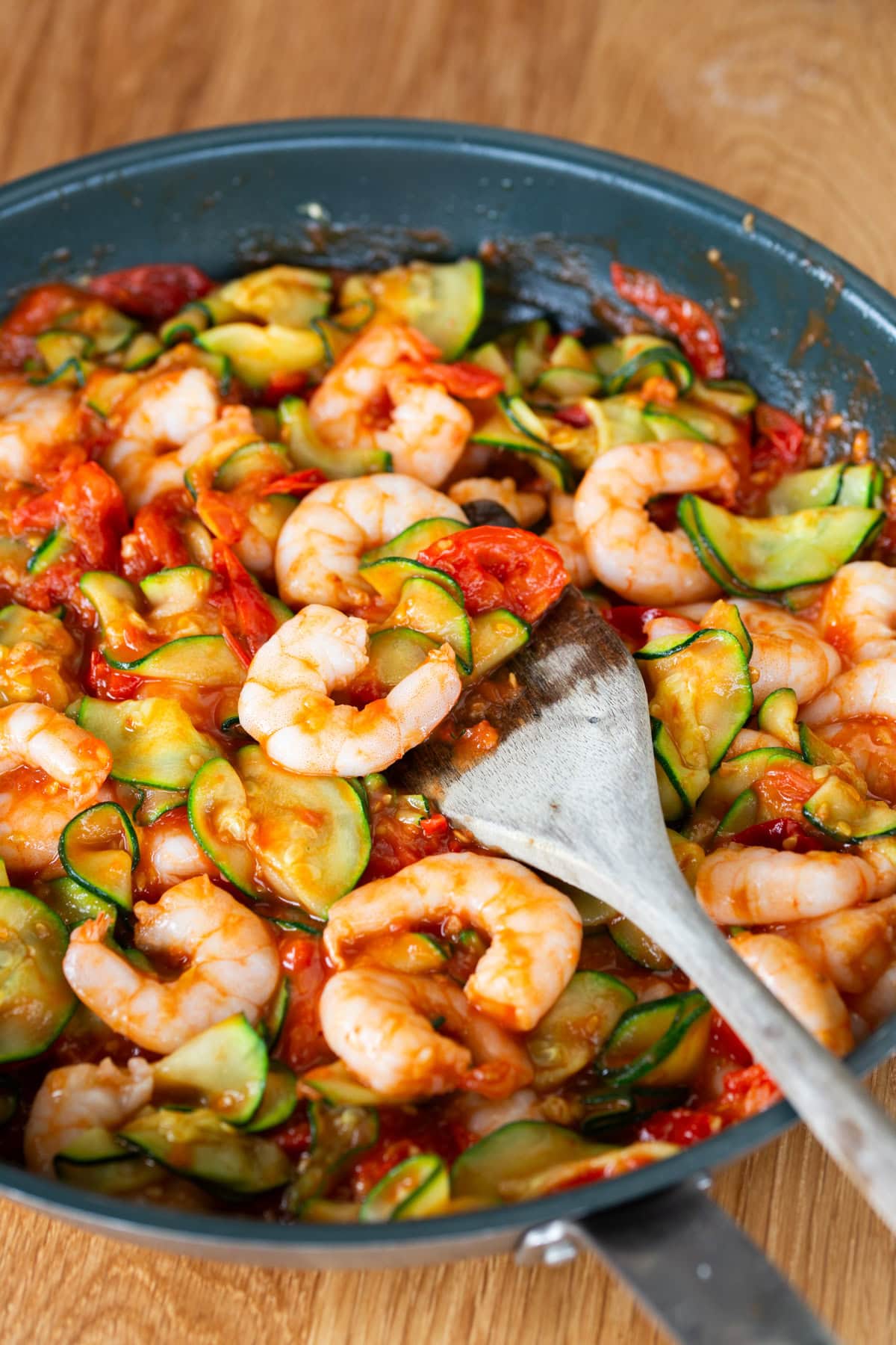 Adding zucchini and shrimps to cherry tomato sauce.