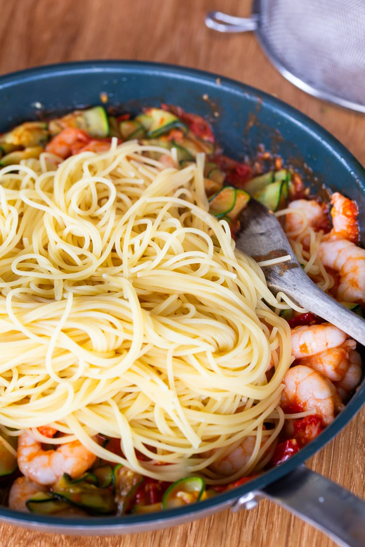 Adding cooked spaghetti to sauce.