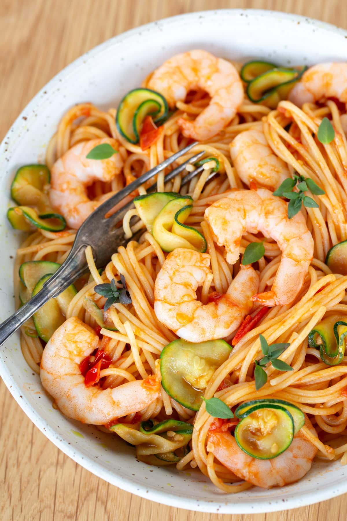 Cherry tomato pasta with shrimp and zucchini on a white plate.