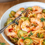 Cherry tomato pasta with shrimp and zucchini on a white plate.