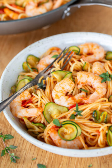 Cherry tomato pasta with shrimp and zucchini on a white plate.