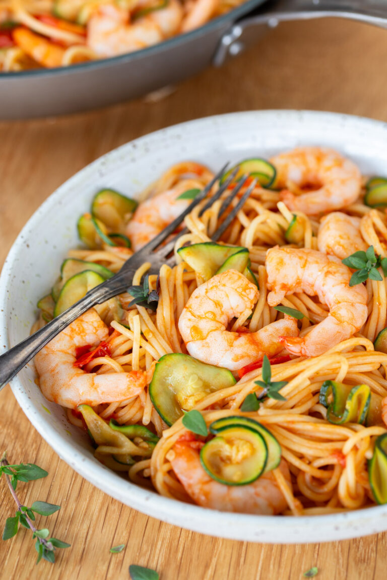 Cherry tomato pasta with shrimp and zucchini on a white plate.