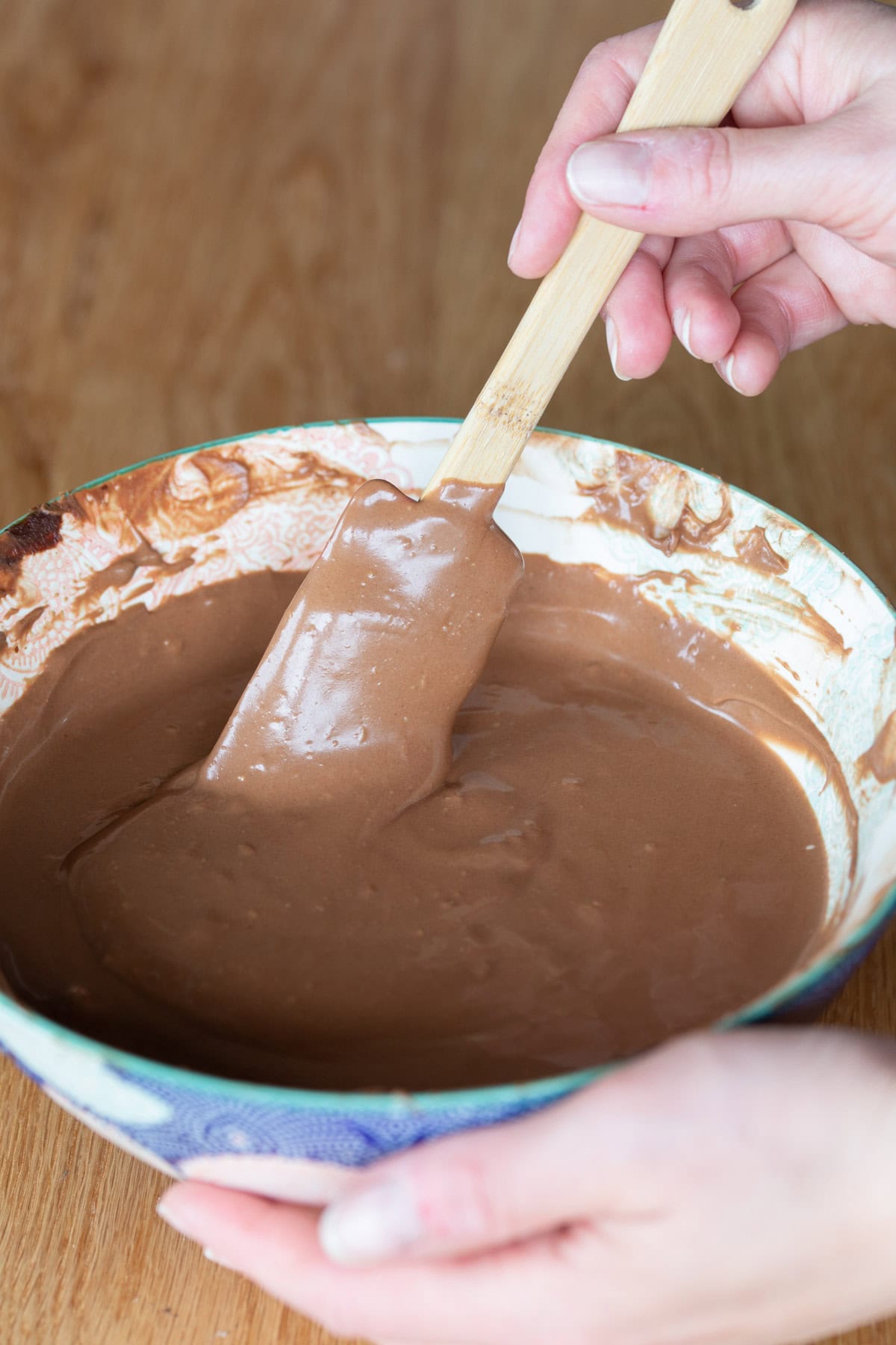 Hand stirring spatula in chocolate cheesecake bowl.