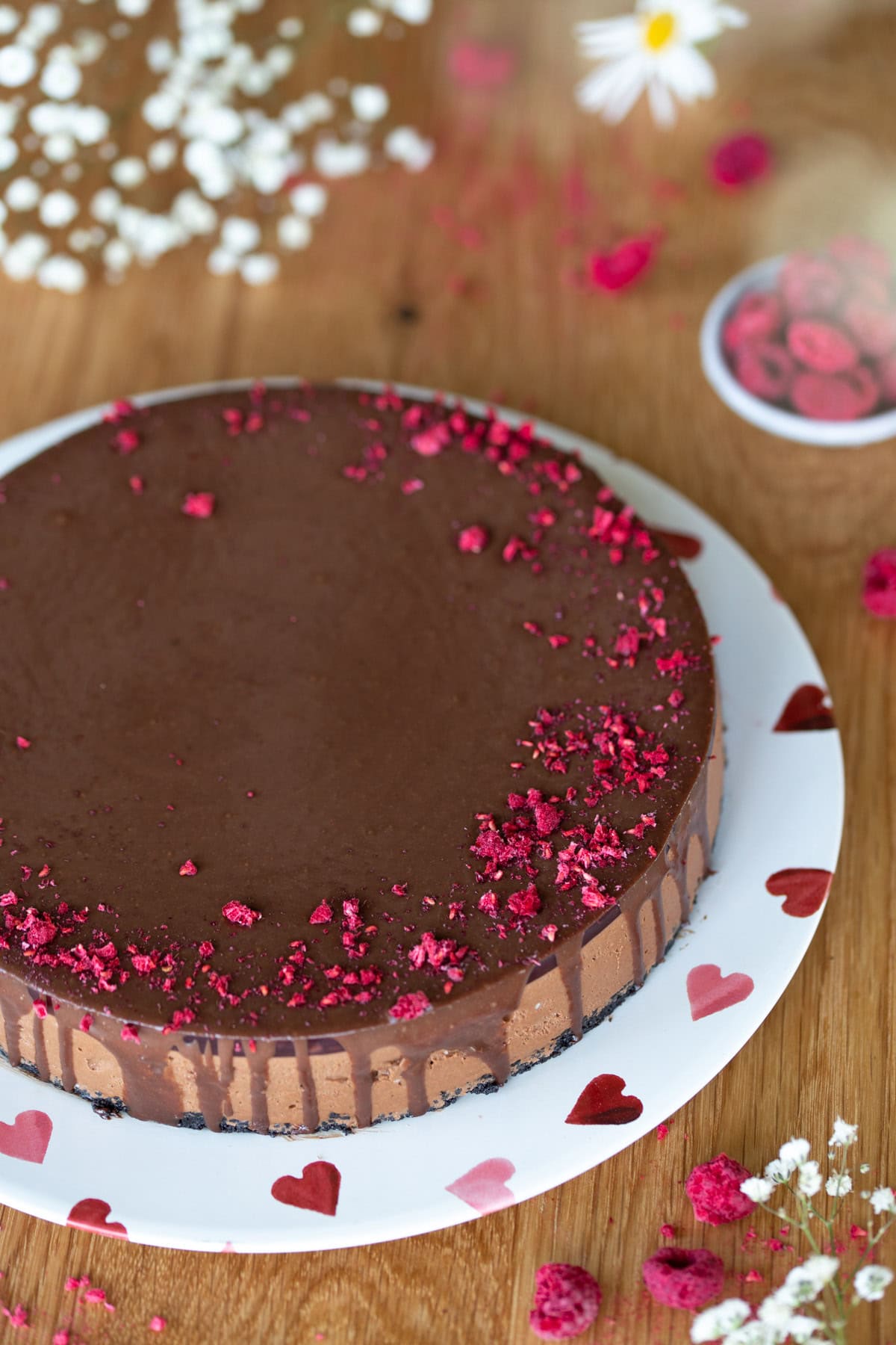 Chocolate raspberry cheesecake covered in chocolate ganache served on a white plate with pink hearts.