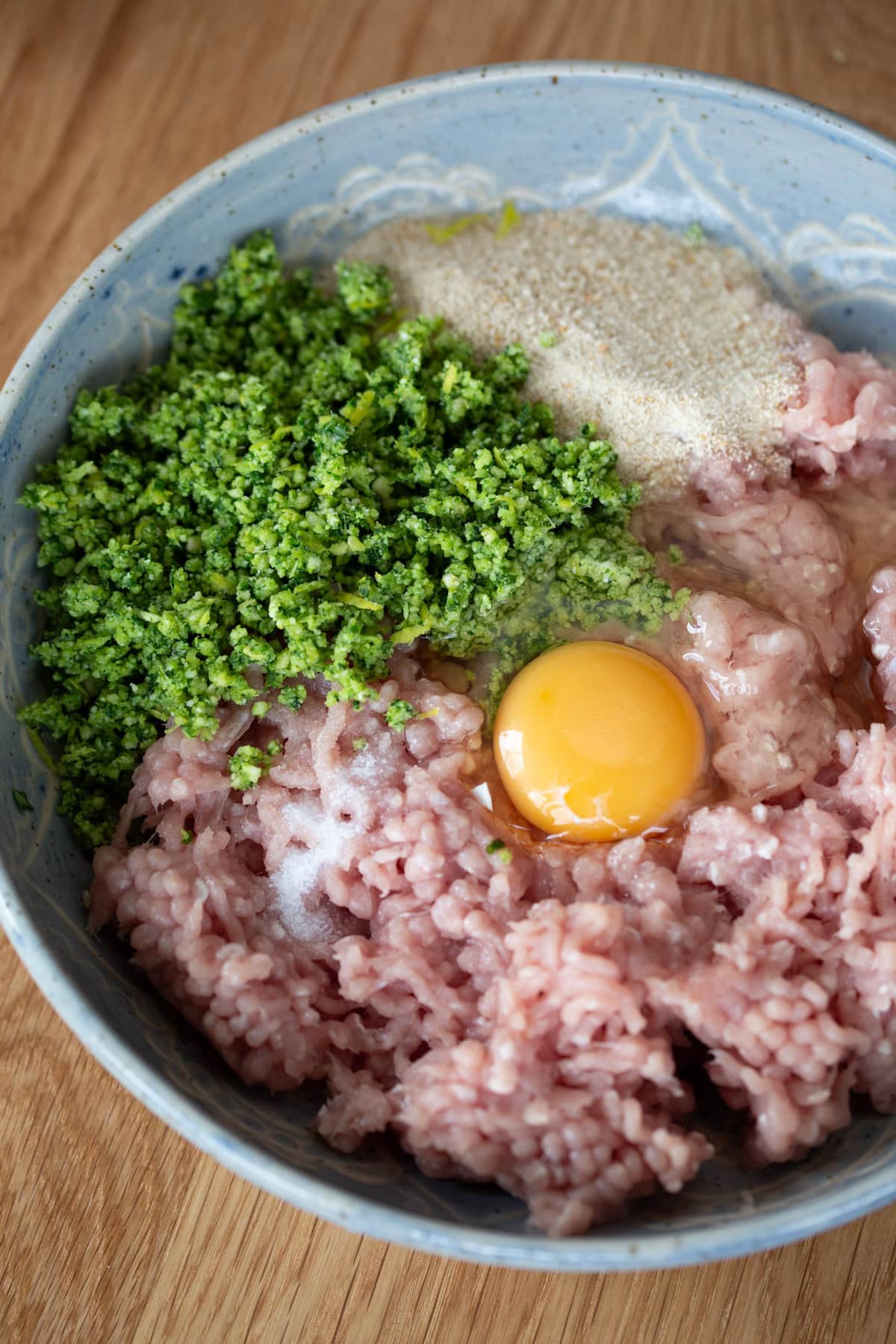 Ground chicken and the other ingredients in a blue bowl.