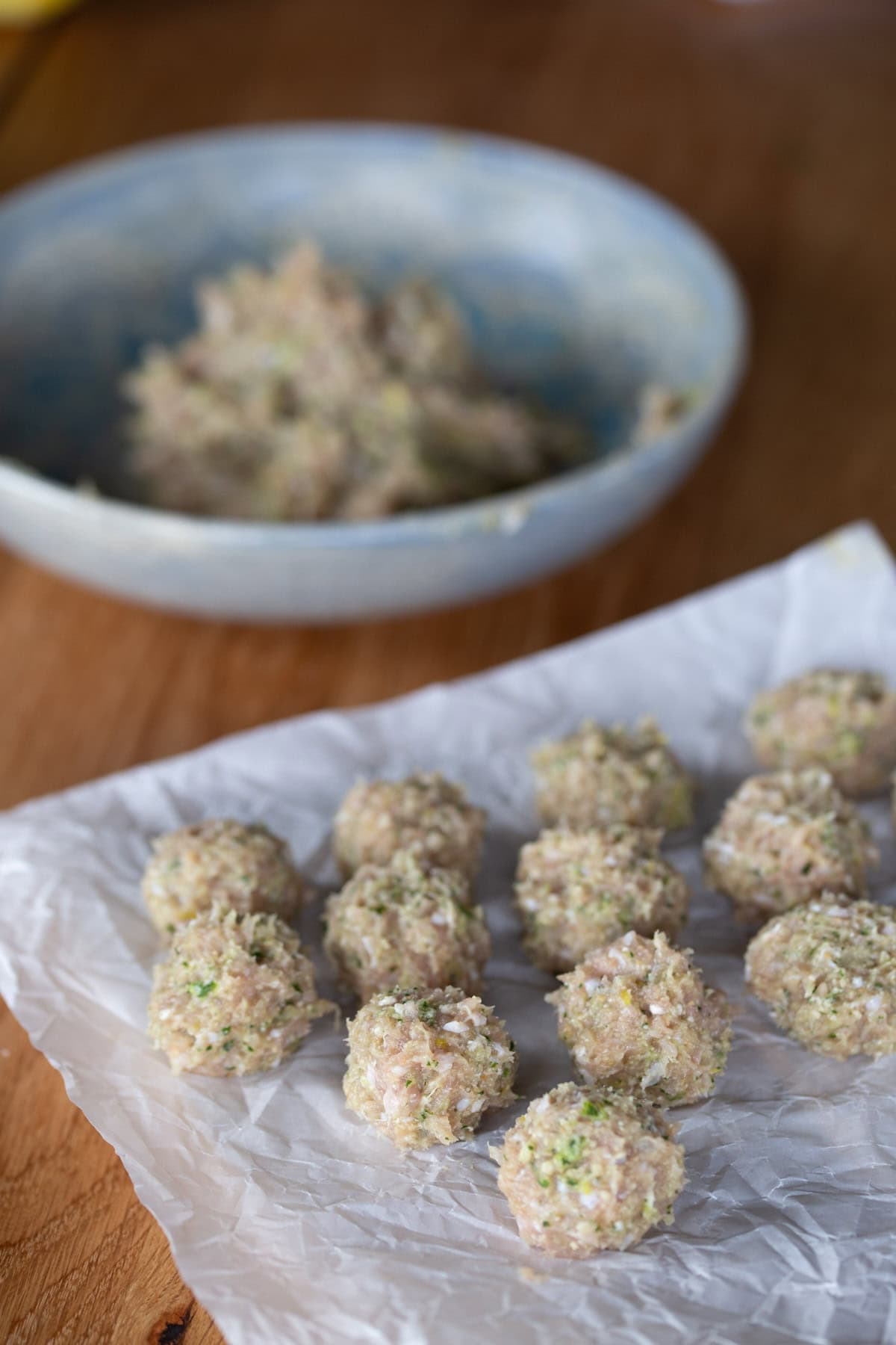 Uncooked formed meatballs on white paper.
