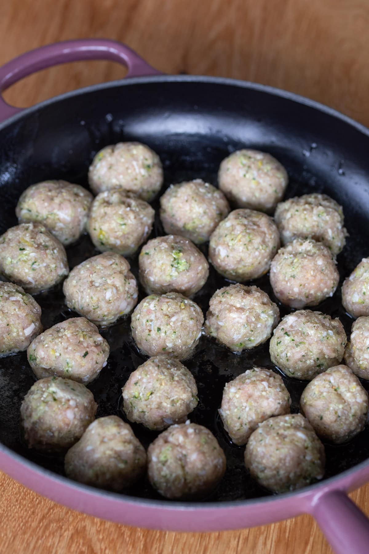 Uncooked meatballs in a cast iron skillet.