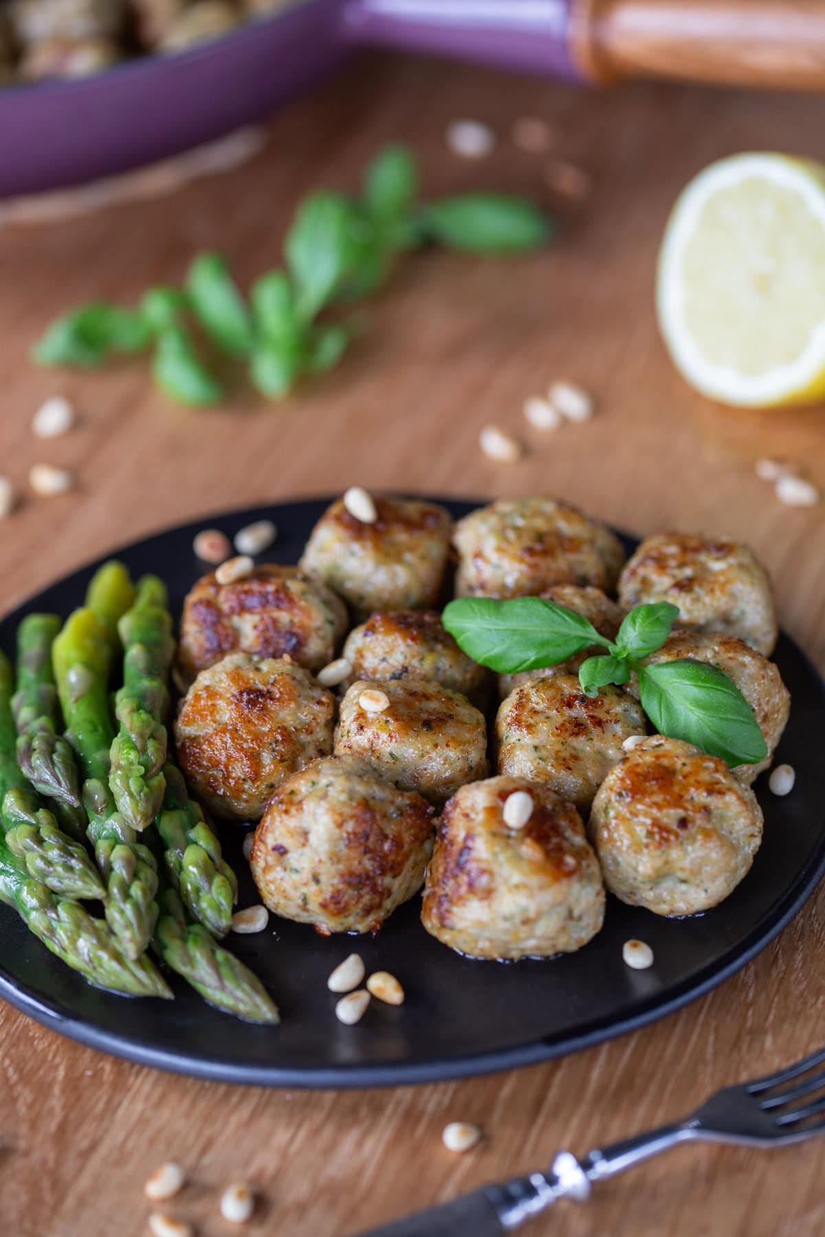 Lemon basil chicken meatballs served with asparagus on a black plate.