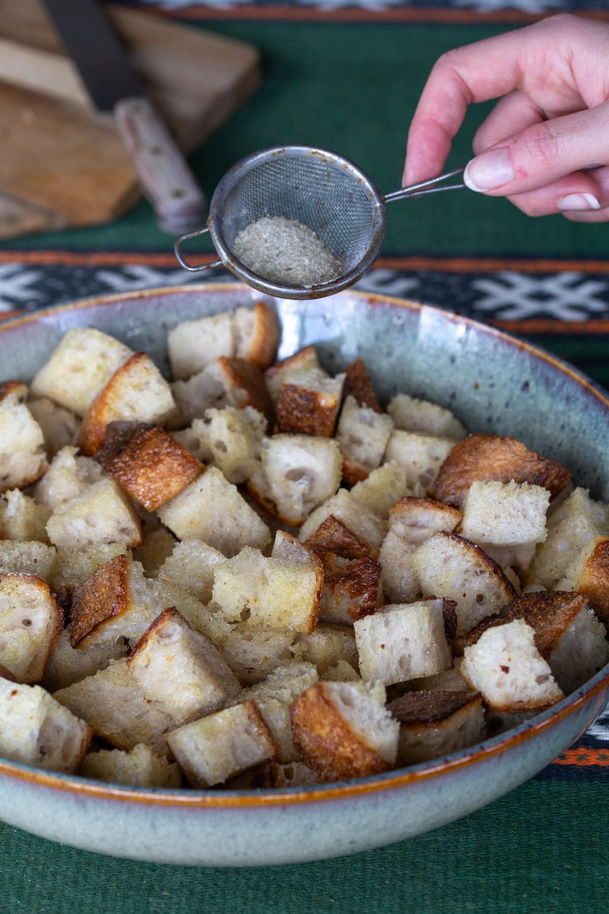 Sprinkling dried herbs over diced sourdough.