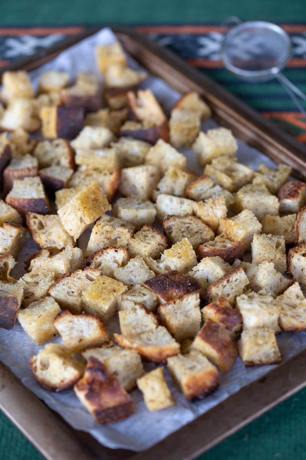 Sourdough bread diced and seasoned on metal tray.