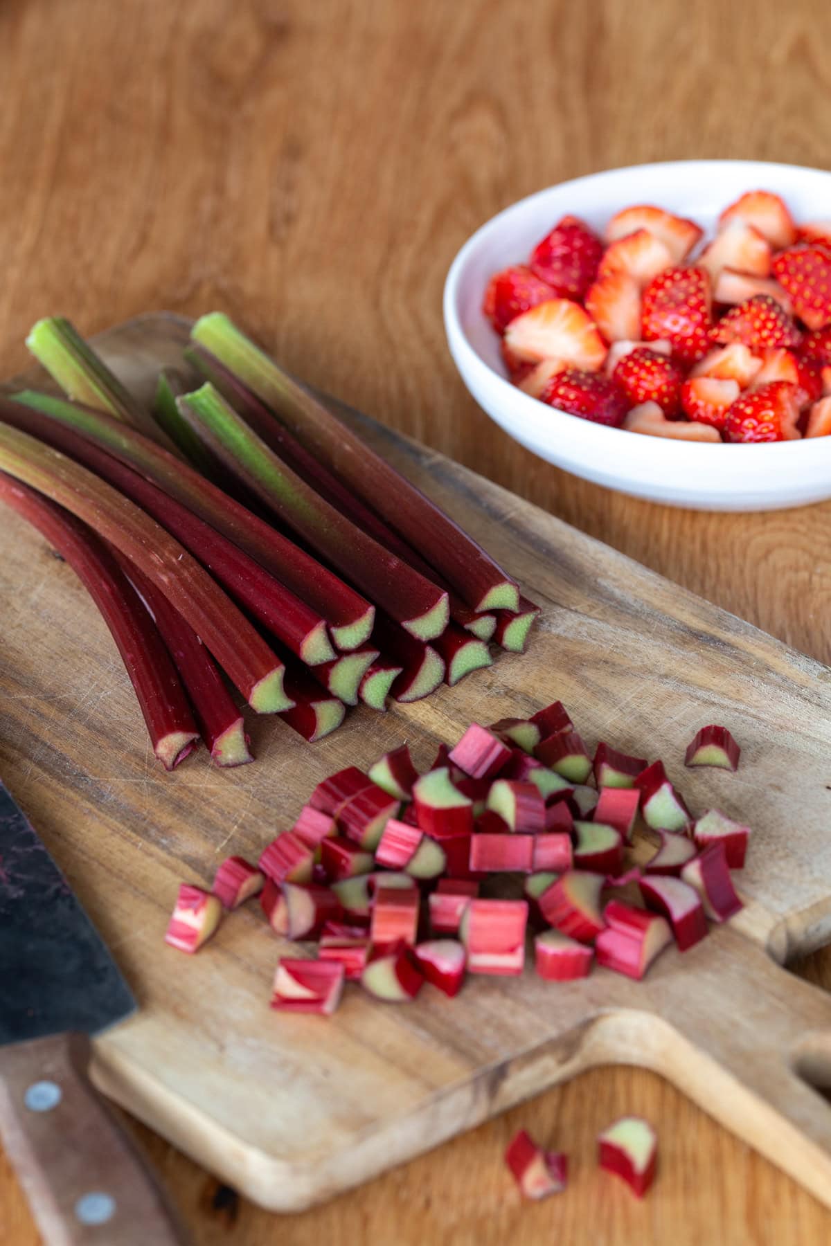 Rhubarb stalks being chopped on a wooden cutting board.