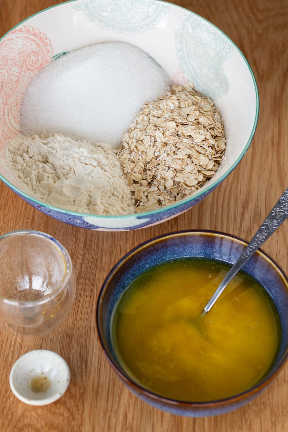 One bowl with melted butter, on bowl with oats, flour and sugar.