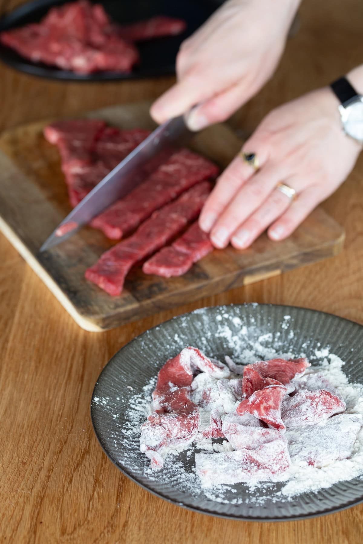 Hands slicing up beef meat, flored meat strips in the foreground.
