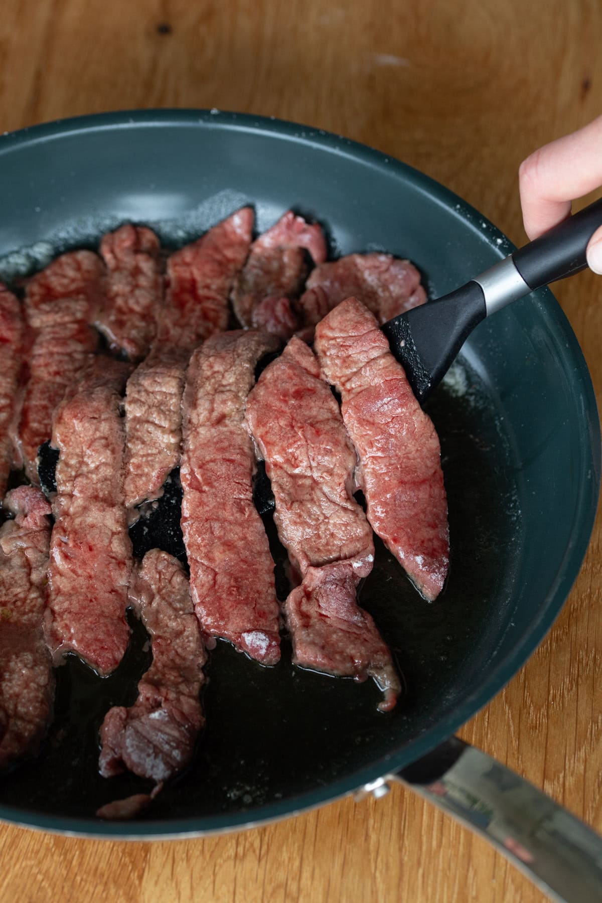 Beef strips being cooked in a pan.
