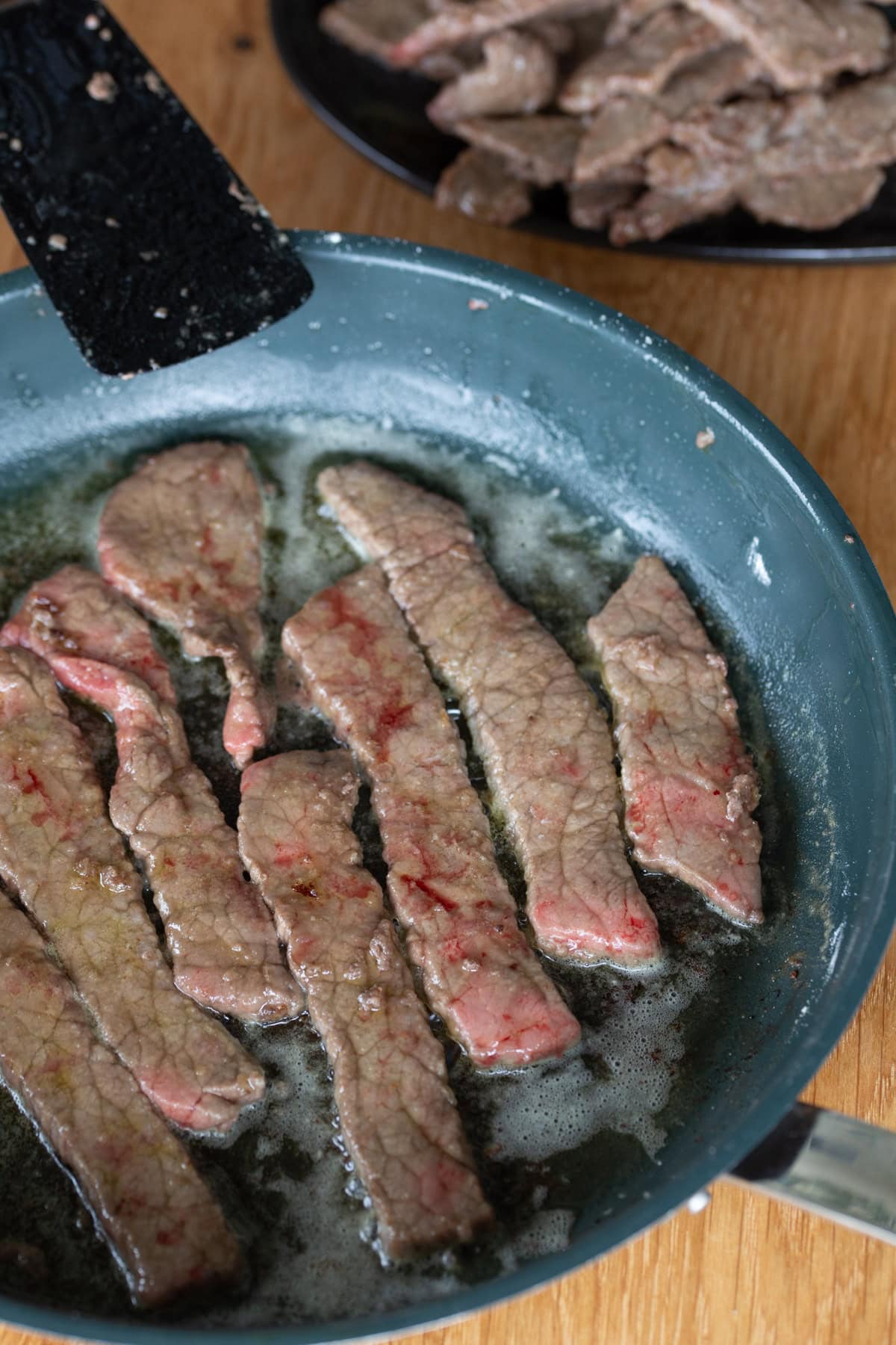 Beef strips being cooked in a pan.