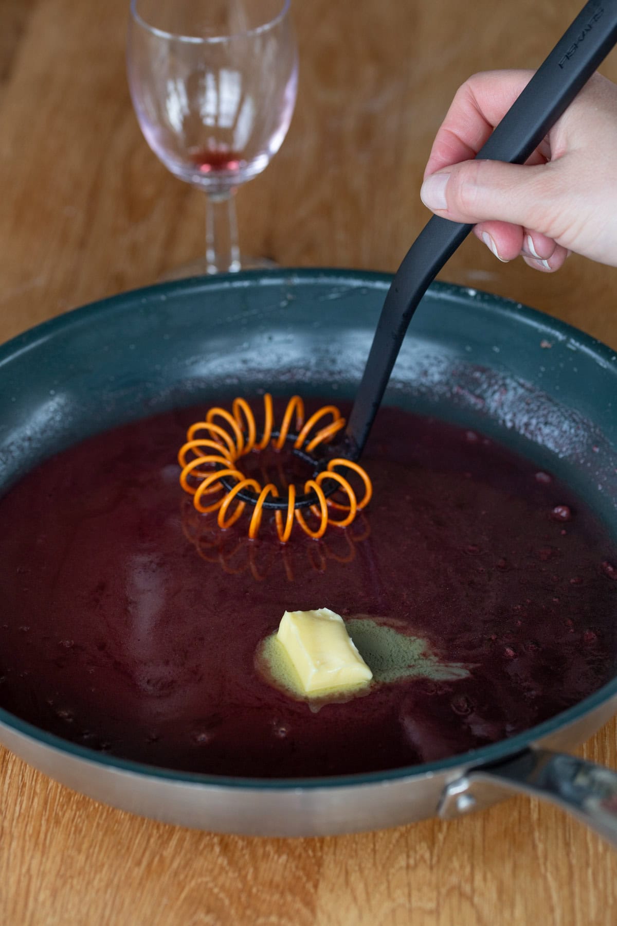 Hand stirring butter into wine reduction.