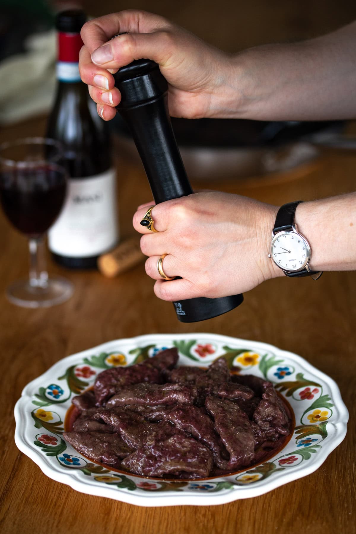 Hands holding a pepper grinder over a portion of meat.