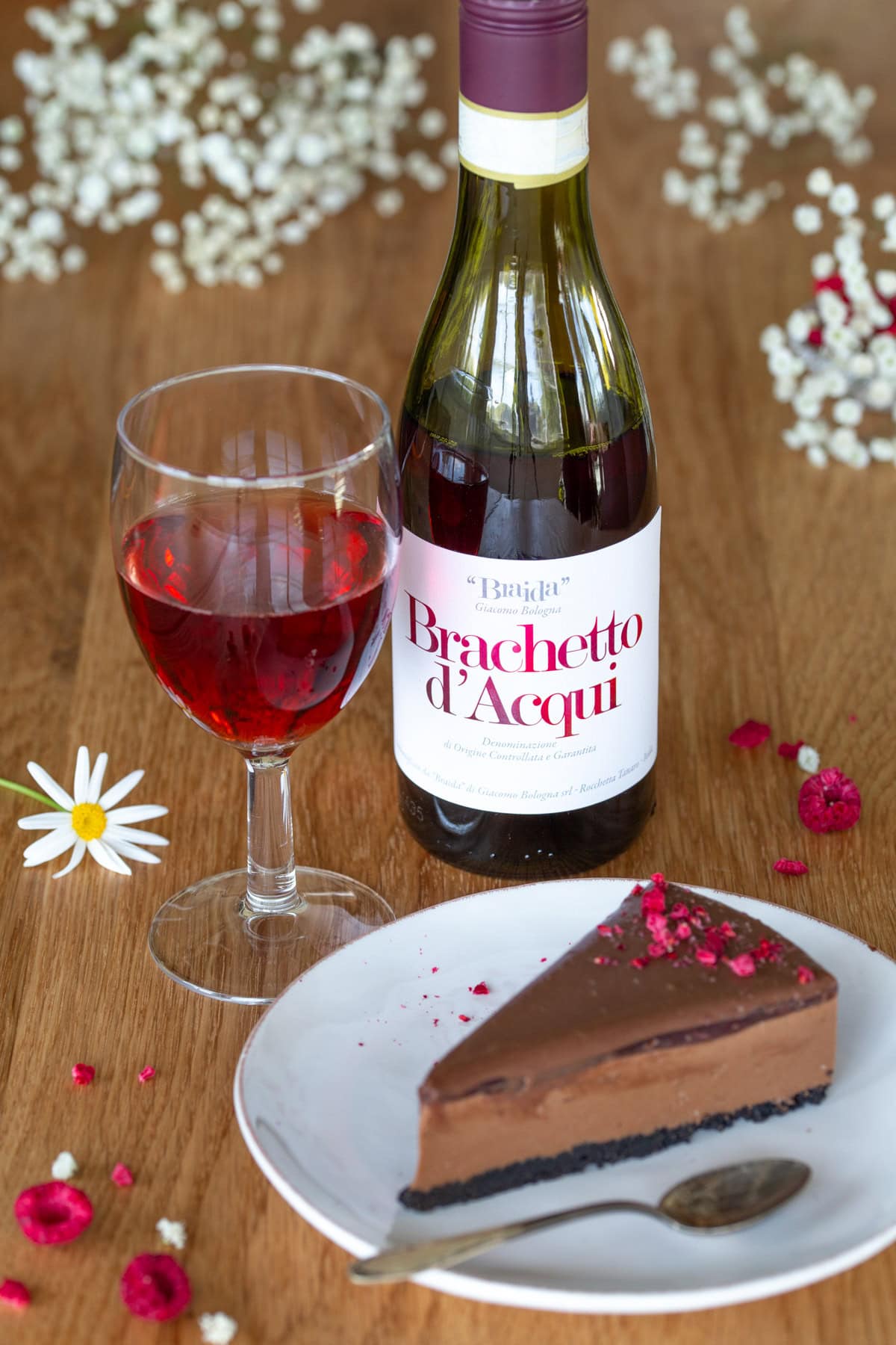 A slice of chocolate cheesecake next to a bottle and glass of Brachetto wine.