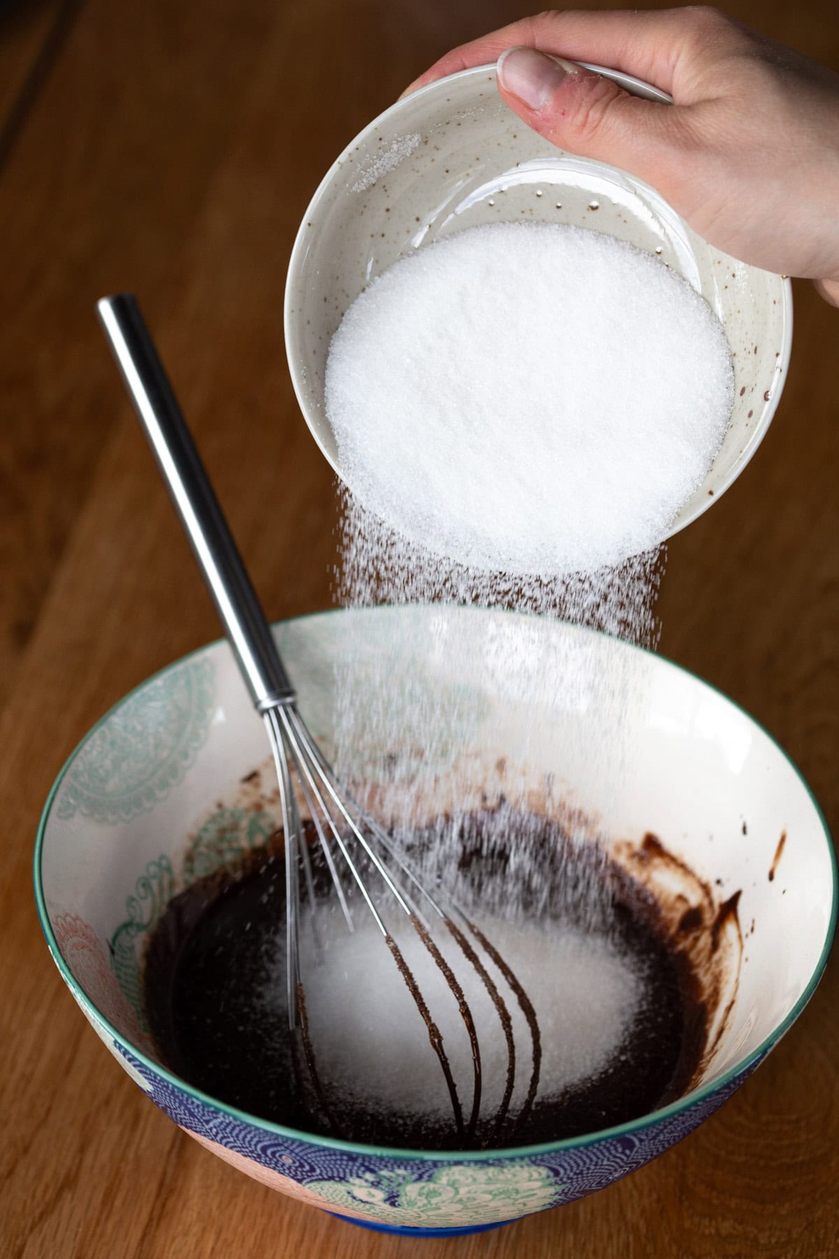 Pouring granulated sugar into cake batter.