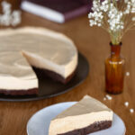 One slice of coffee mousse cake on a plate, rest of the cake in the background.
