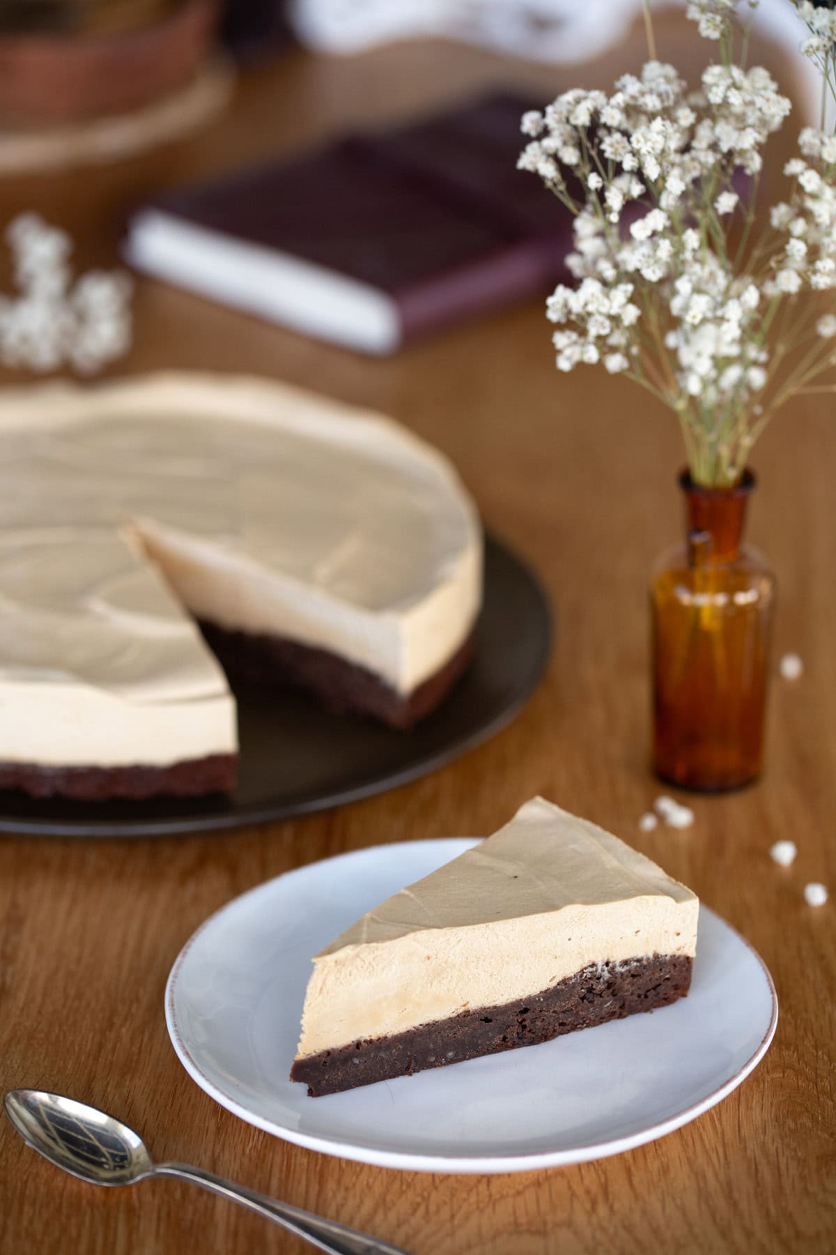 One slice of coffee mousse cake on a plate, rest of the cake in the background.