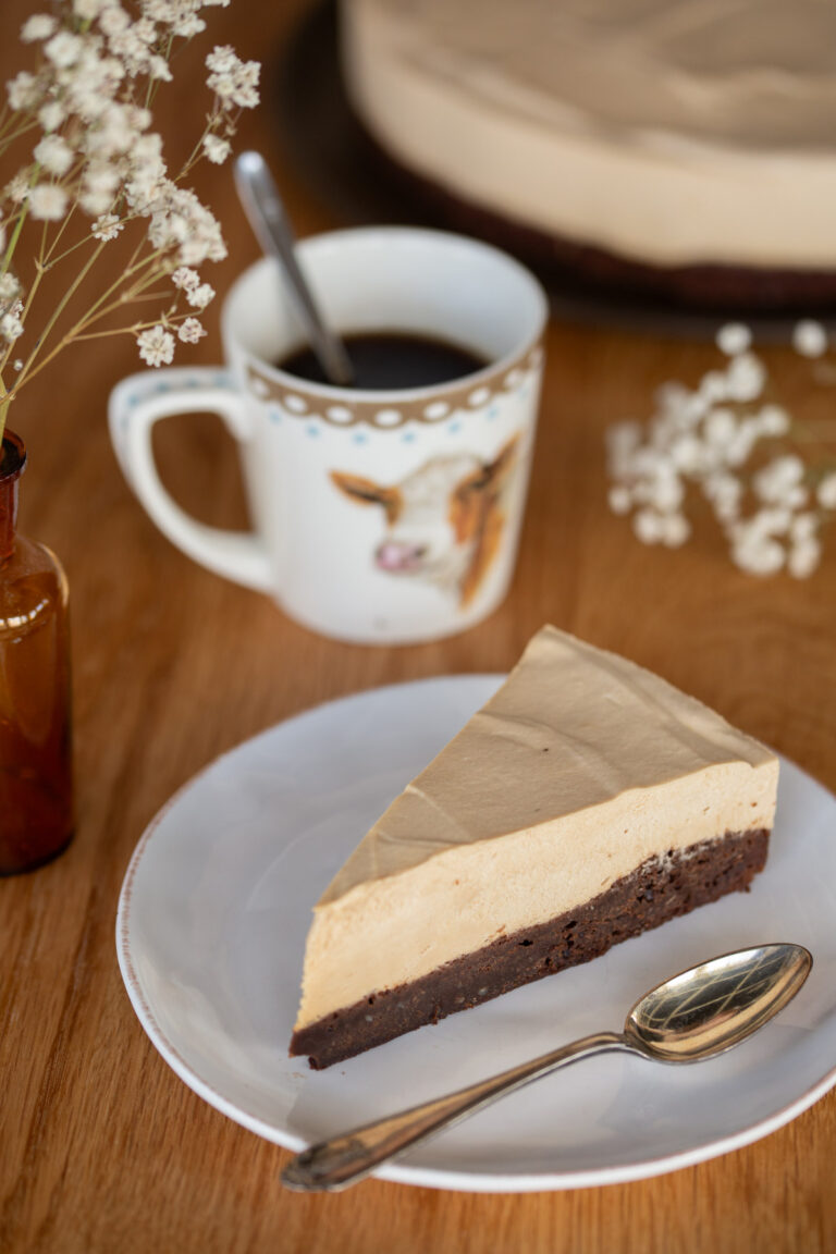 One slice of coffee mousse cake on a plate, a mug of coffee in the background.