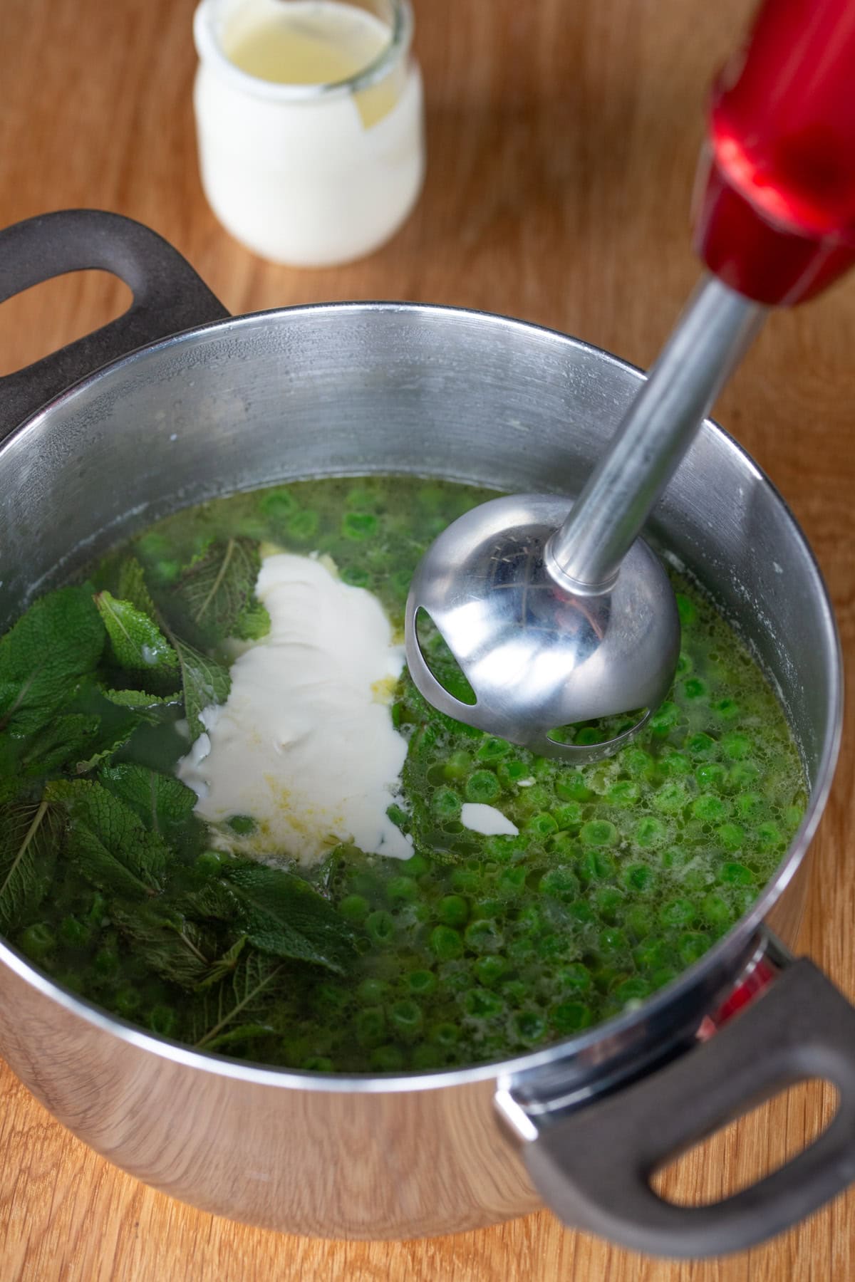 Hand blender being lowered into pot full of peas and cream.