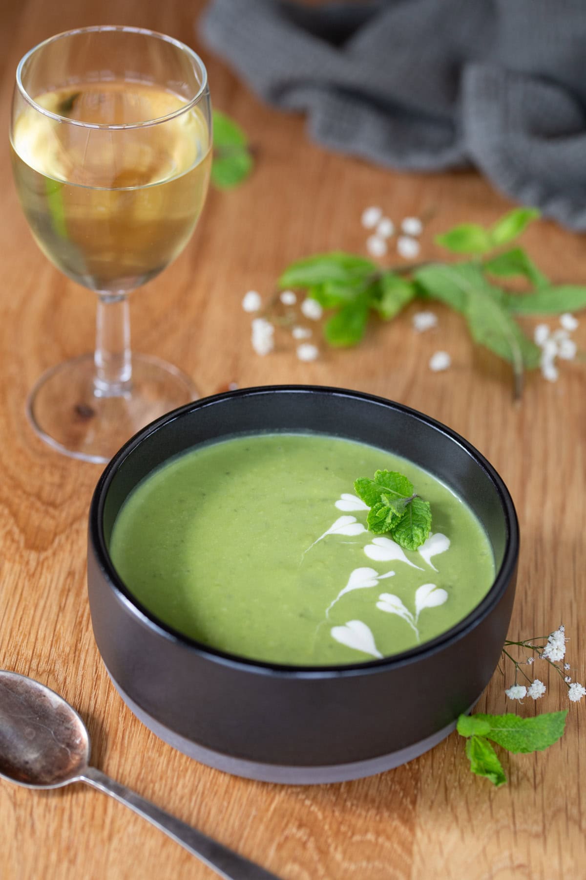 A black bowl of pea soup with mint, glass of white wine aside.