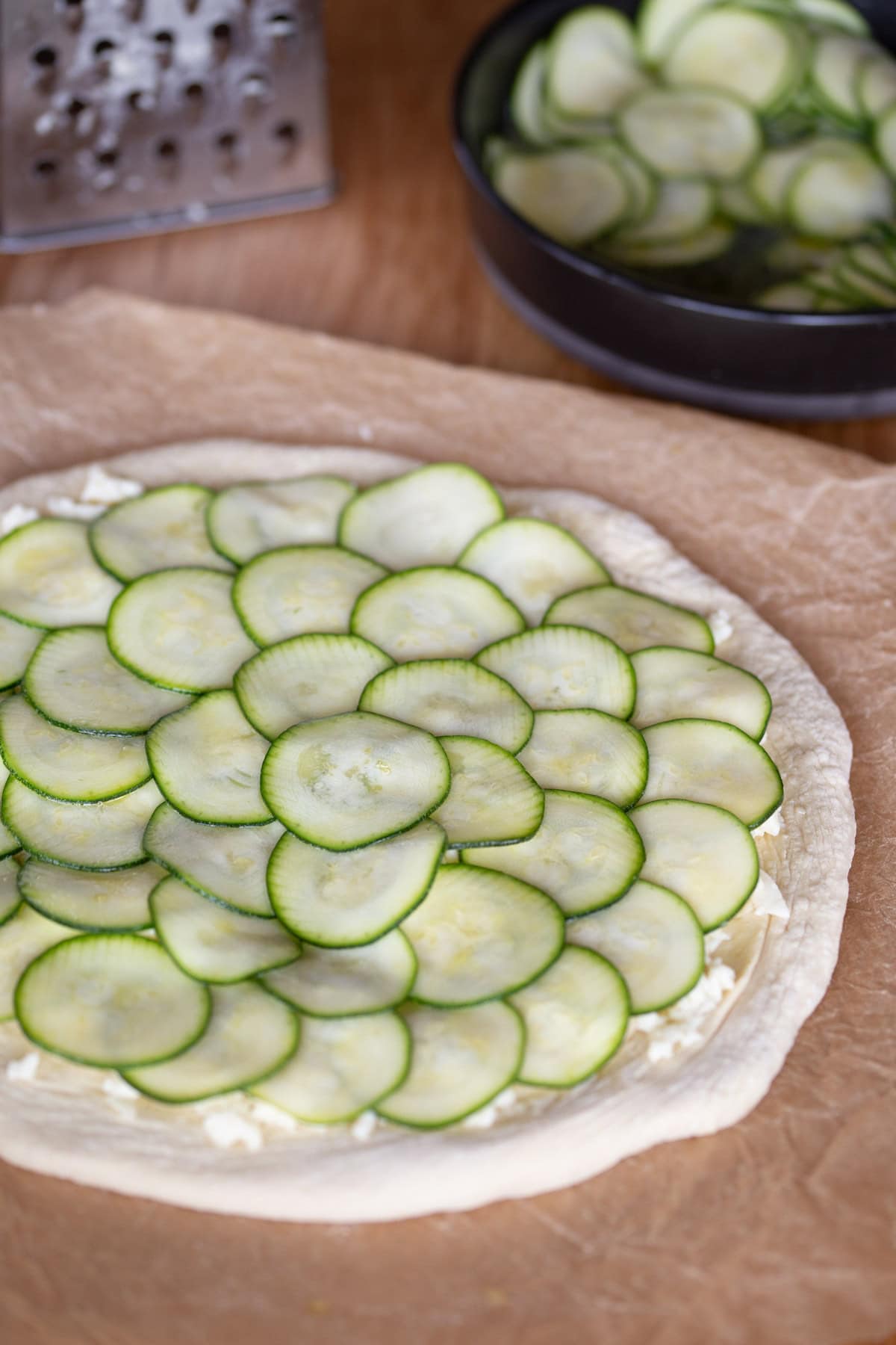 Layering marinated zucchini over unbaked pizza dough.