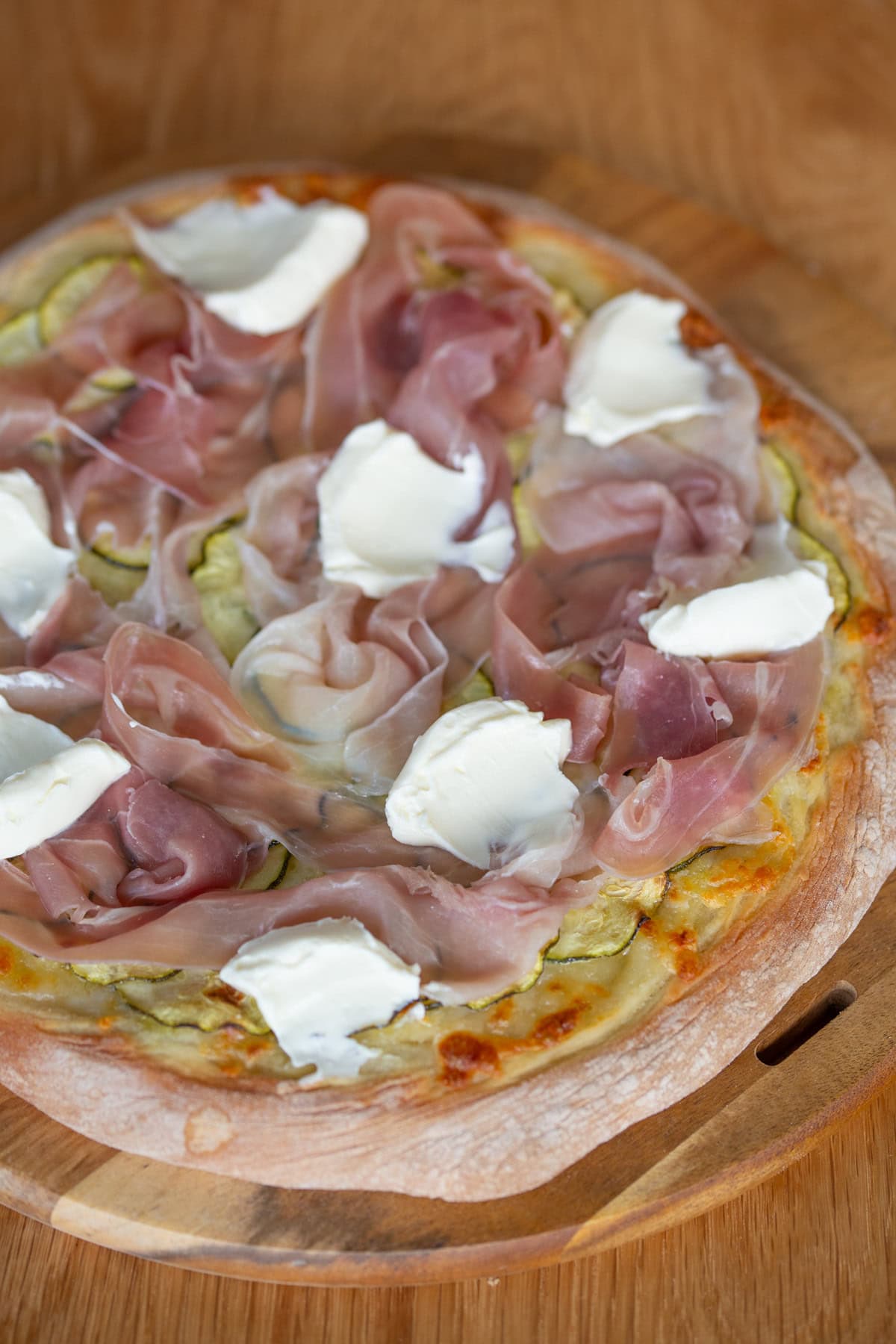 Pizza with marinated zucchini, prosciutto and cream cheese dollops closeup.