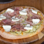 Pizza with marinated zucchini, prosciutto and cream cheese dollops.