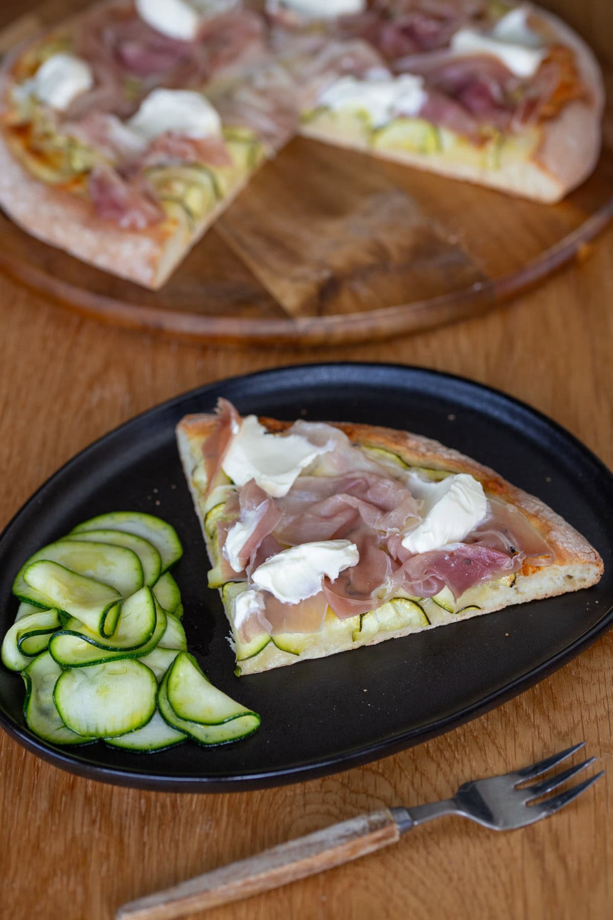 A slice of pizza with marinated zucchini and prosciutto served with a side of marinated zucchini.