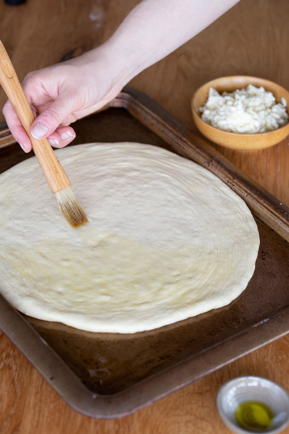 Bushing olive oil over stretched pizza dough with a pastry brush.