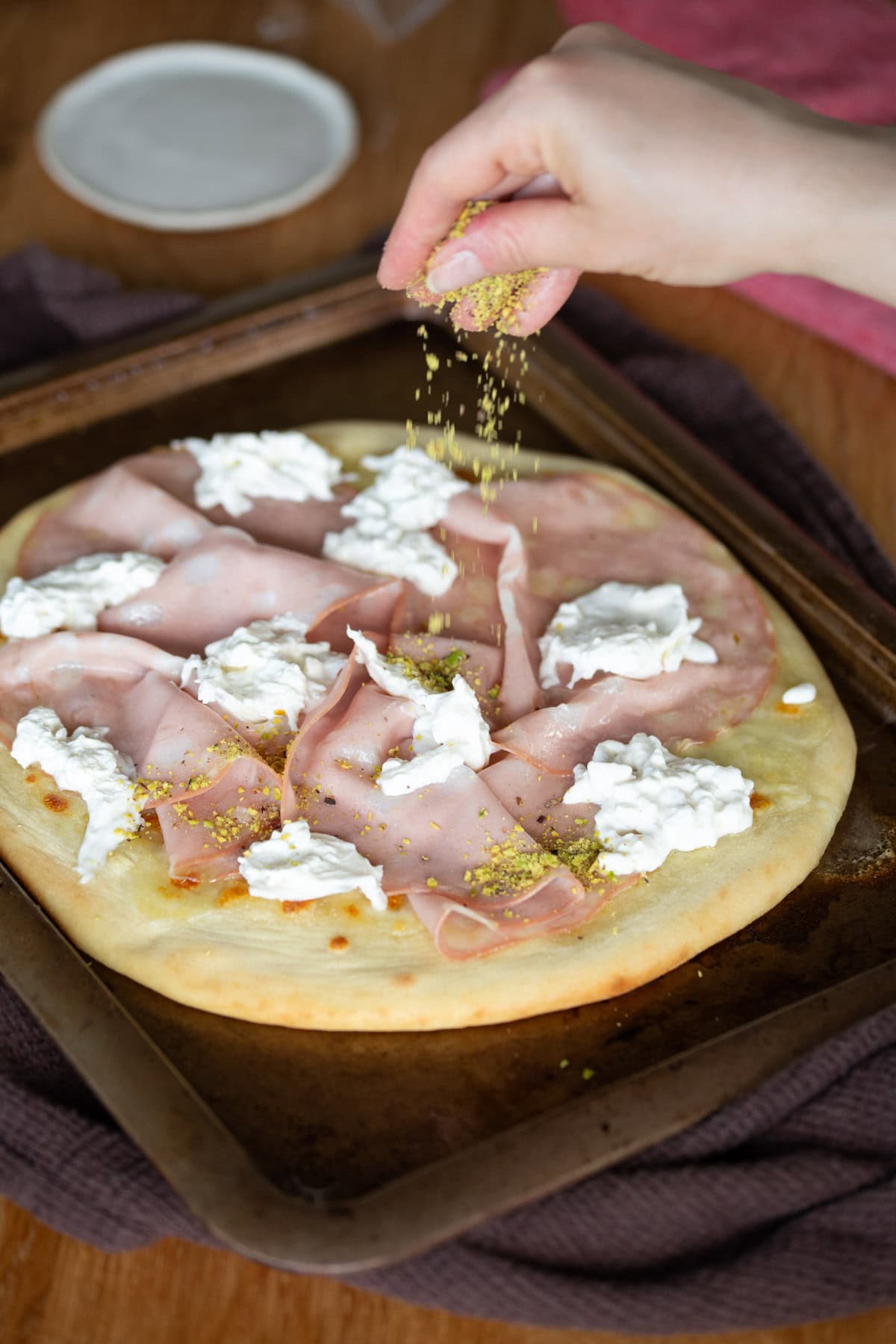 Hand sprinkling crushed pistachios over mortadella pizza.