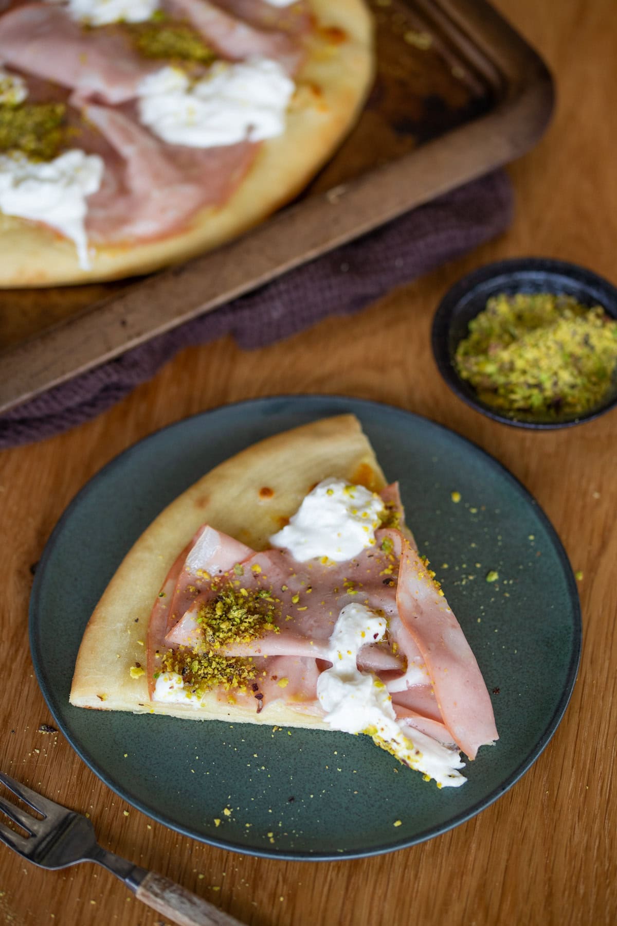One slice of mortadella pizza on a green plate.
