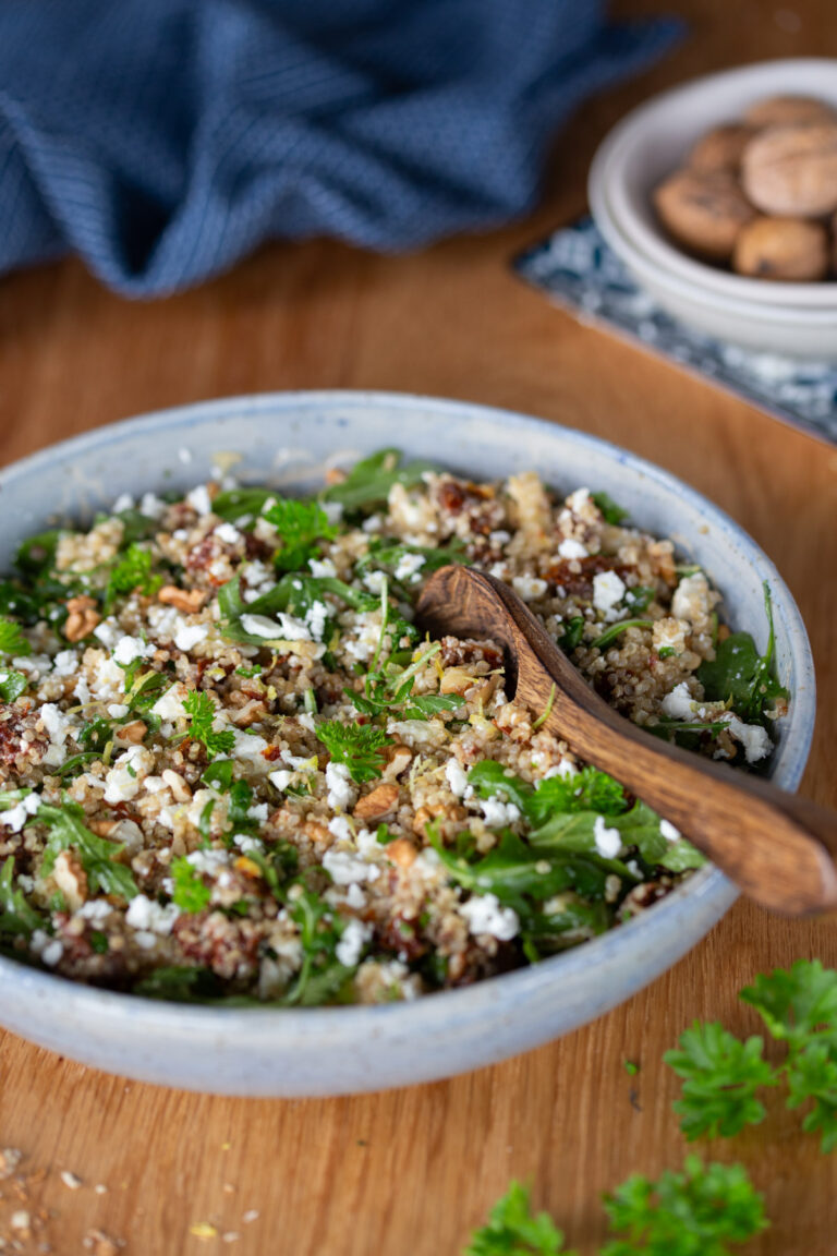 Quinoa salad with sun-dried tomatoes, feta and walnuts in a light blue bowl.