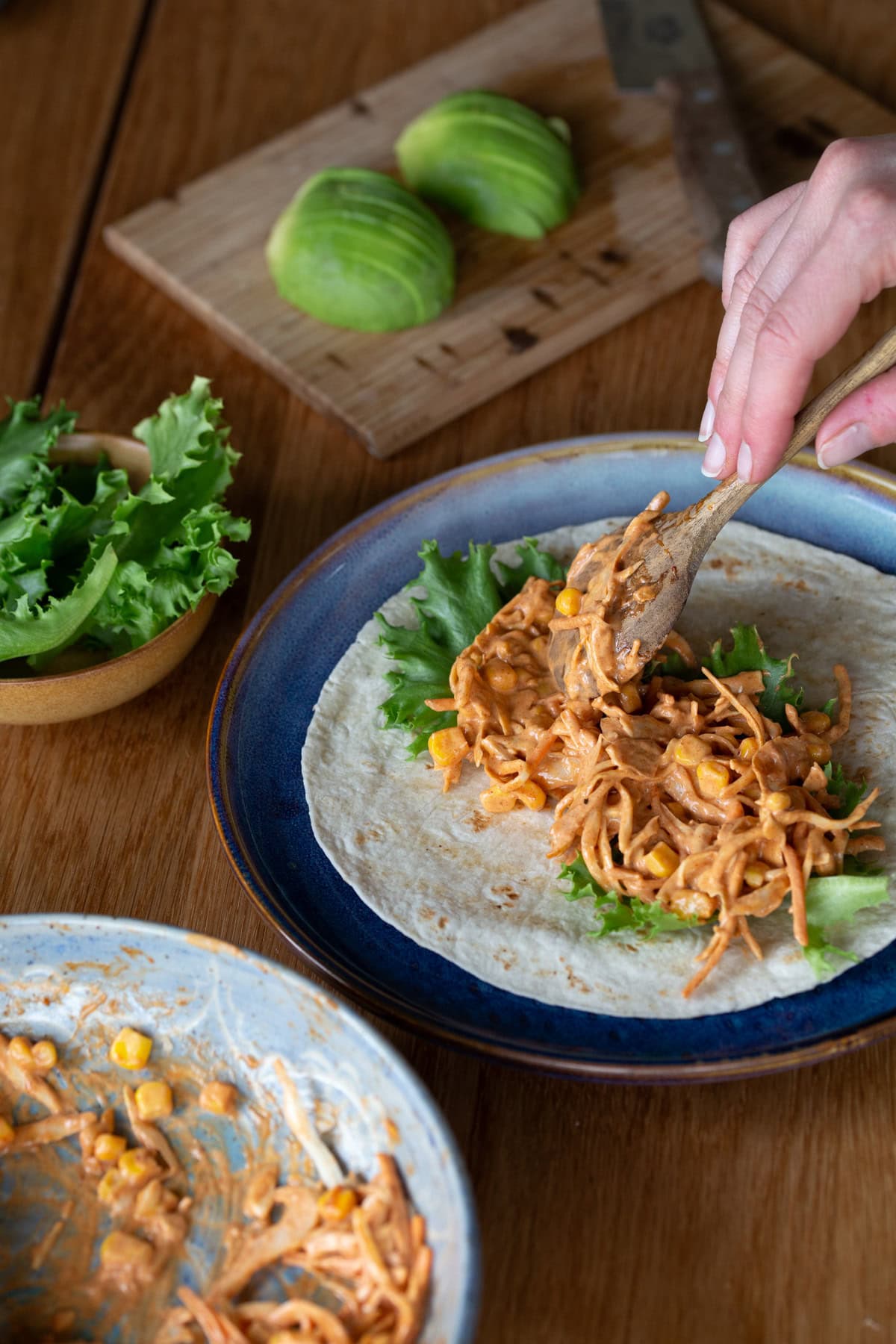 Hand adding smokey cornslaw to wrap bread with lettuce.