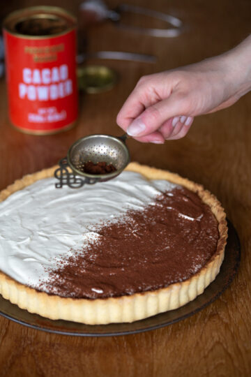 Hand sprinkling cocoa over tiramisu pie.