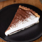 One slice of tiramisu pie on a dark plate.
