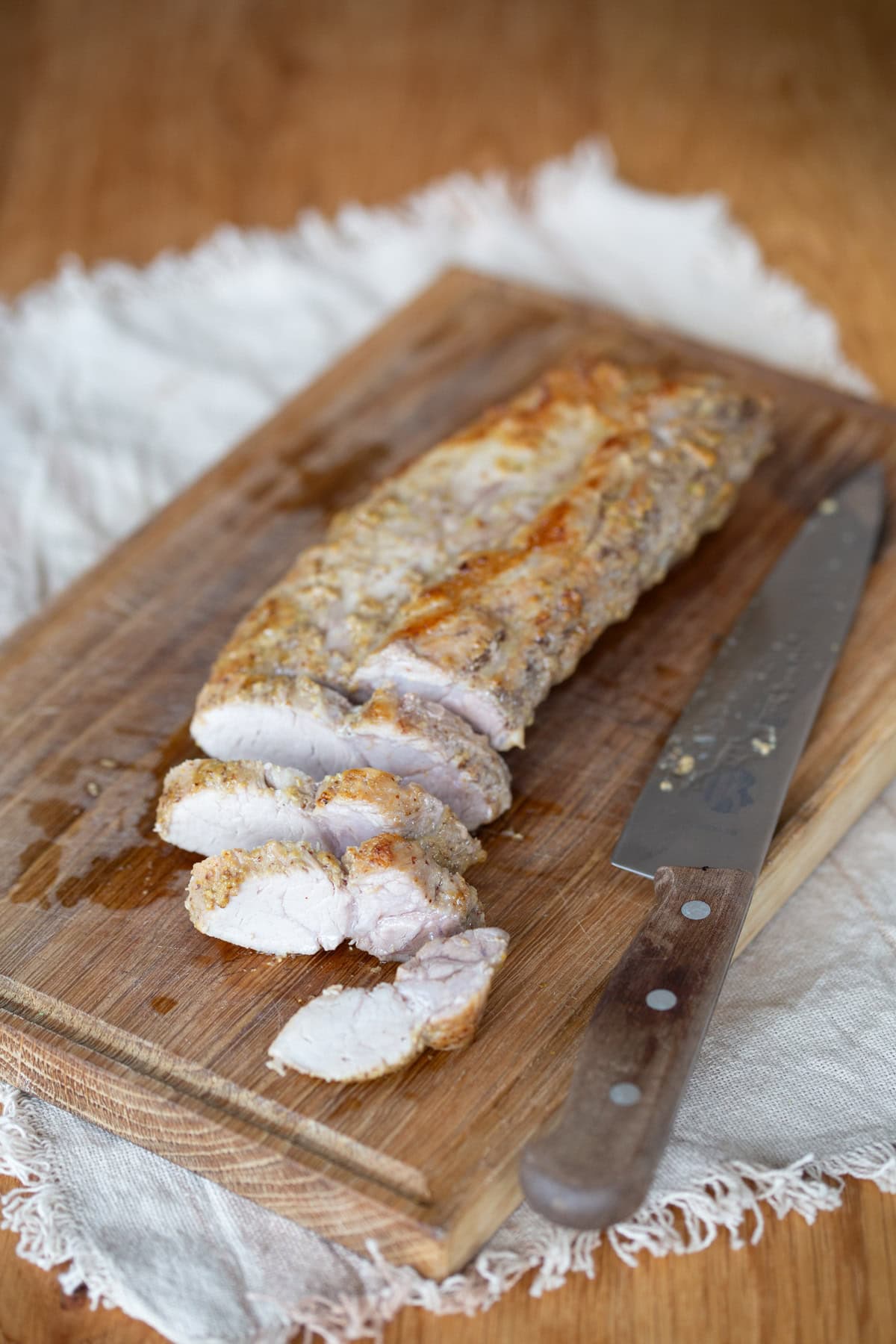Slicing baked pork loin on a wooden board.