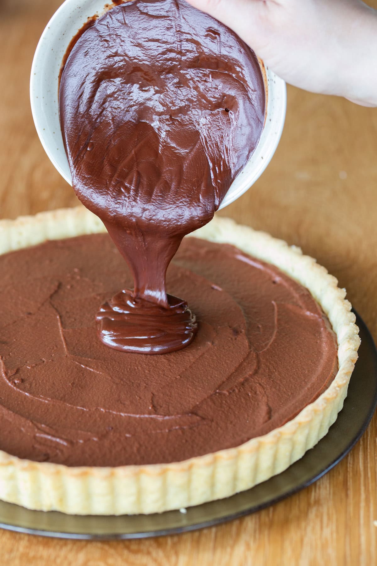 Pouring chocolate and coconut oil mixture over tart filling.