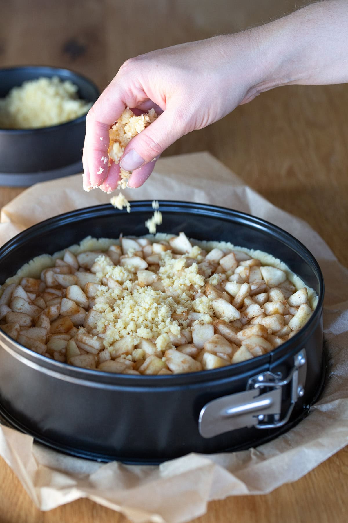 Hand scattering unbaked pie dough crumbles over pie filling.