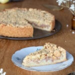 A slice of Polish apple pie szarlotka on a white ceramic plate, pie in the background.