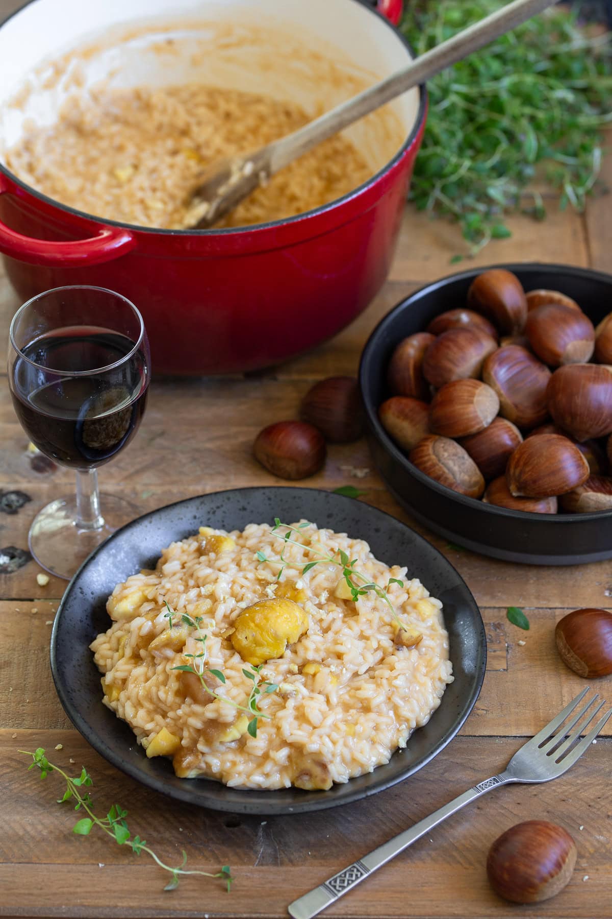 A portion of chestnut risotto, a bowl of chestnuts and the pot with more risotto in the background.