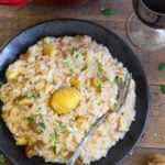 Closeup of a portion of chestnut risotto with toma on a black plate.