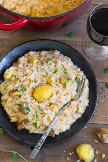 Closeup of a portion of chestnut risotto with toma on a black plate.