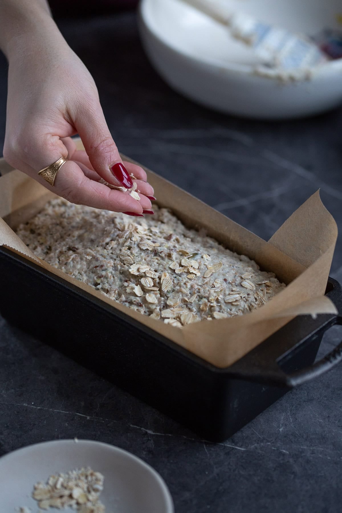 Scattering rolled oats over unbaked bread loaf.