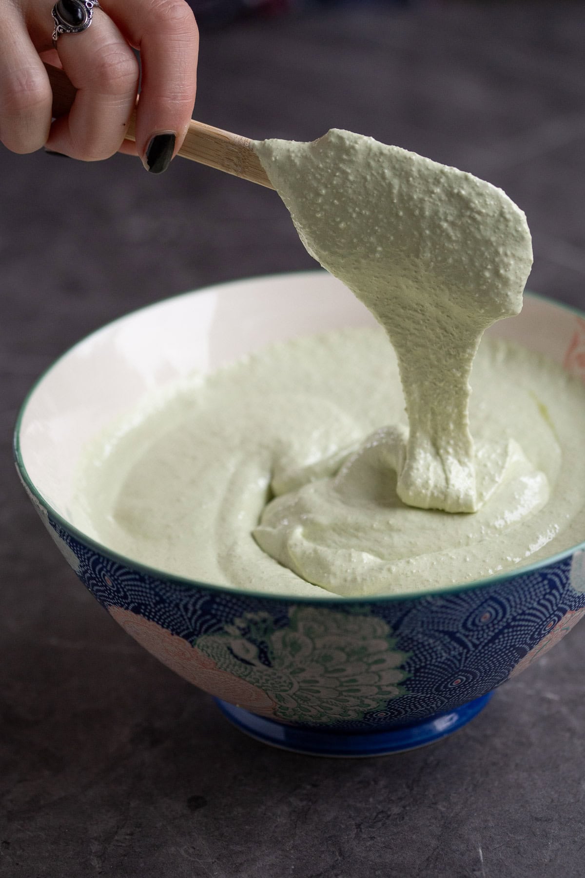 Lifting macarons batter with a spatula to show ribbony texture.