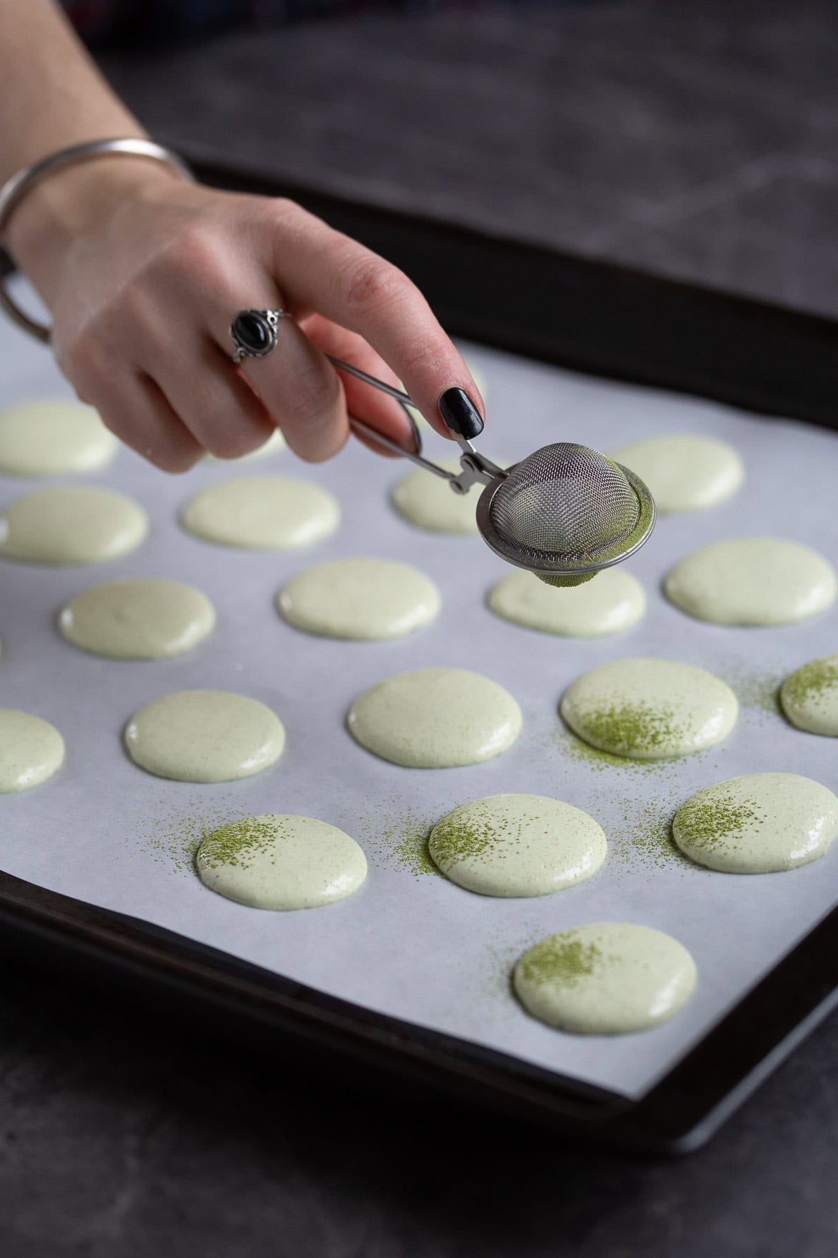 Dusting raw macarons with matcha powder.